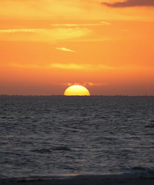 Golden sun setting over a calm ocean beneath an orange sky.